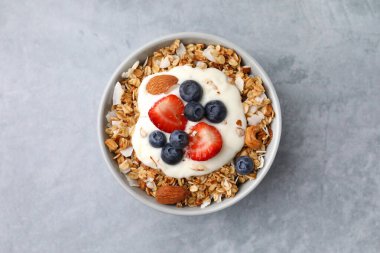 Lezzetli granola, yoğurt ve açık gri masada taze böğürtlen, üst manzara. Sağlıklı kahvaltı.