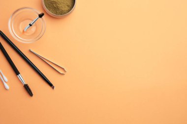 Turuncu arkaplan üzerinde kaş kına ve profesyonel araçlar ile düz kompozisyon, metin için boşluk