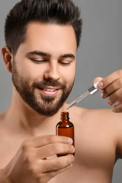 Handsome man with cosmetic serum in hands on grey background