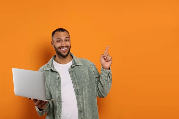 Smiling young man with laptop near orange wall, space for text