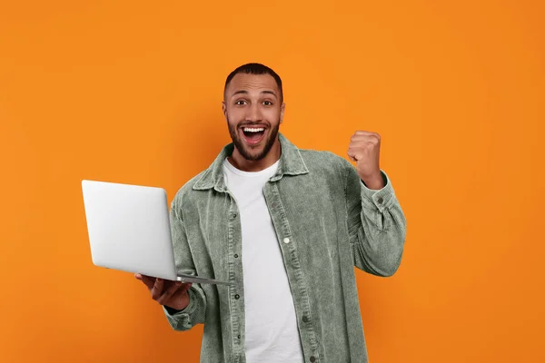 Happy young man with laptop on orange background