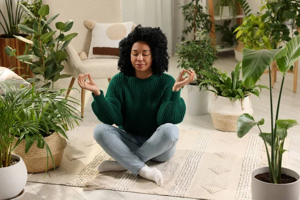 Relaxing atmosphere. Woman meditating near potted houseplants in room