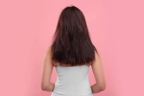 Woman with damaged hair on pink background, back view