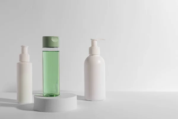 Bottles with different cosmetic products and podium on white background, space for text