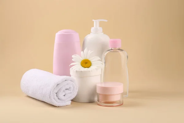 Different skin care products for baby, flower and towel on beige background