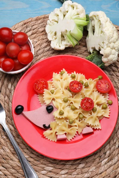 Creative serving for kids. Plate with cute hedgehog made of delicious pasta, sausages and tomatoes on light blue wooden table, flat lay