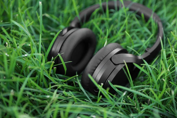 Black wireless headphones on green grass outdoors, closeup