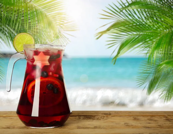 Refreshing Red Sangria on wooden table near sea, space for text