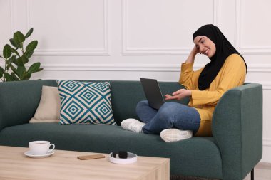 Başörtülü Müslüman kadın içeride bilgisayarında görüntülü konuşma yapıyor. Metin için boşluk