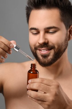 Gri arka planda kozmetik serumu olan yakışıklı bir adam.