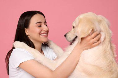 Mutlu kadın pembe arka planda şirin Labrador Retriever köpeğiyle oynuyor. Sevimli hayvan.