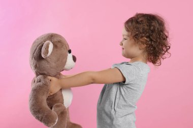 Pembe arka planda oyuncak ayısı olan sevimli küçük bir kız.