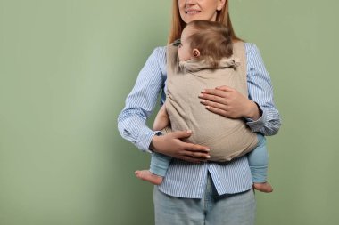 Anne, zeytin arka planında çocuğunu askıda (bebek taşıyıcısı) tutuyor.
