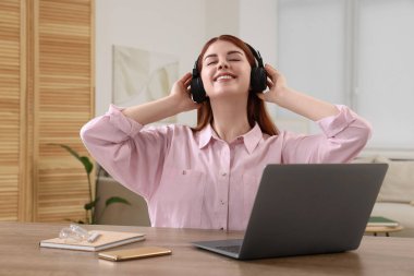 Kulaklıklı mutlu kadın ahşap masada müzik ve laptop dinliyor.