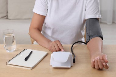 İçerideki ahşap masada kan basıncını ölçen kadın, yakın plan.