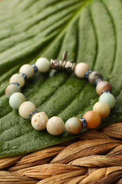 Hasır yüzeyinde değerli taşlar ve yeşil yaprak olan güzel bilezik.