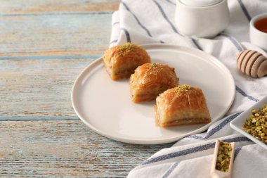 Açık mavi ahşap masada fıstıklı enfes tatlı baklava, metin için yer var.