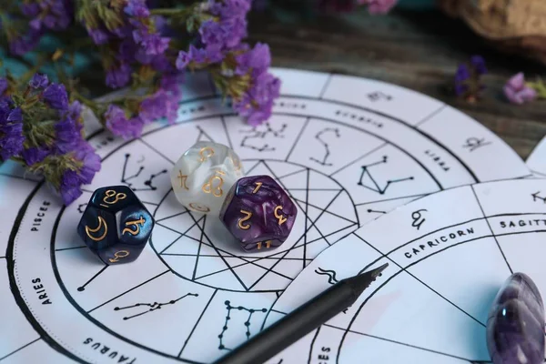 Zodiac wheels, flowers and astrology dices on wooden table, closeup
