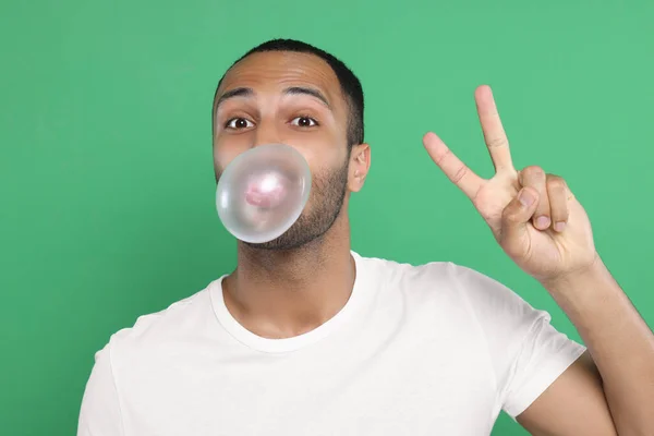 Portrait Young Man Blowing Bubble Gum Showing Peace Gesture Green — Stock Photo, Image