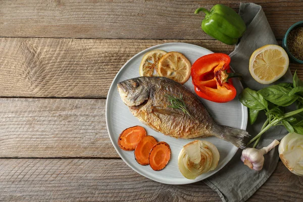 Delicious dorado fish with vegetables and herbs served on wooden table, flat lay. Space for text