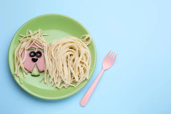 Creative serving for kids. Plate with cute dog made of tasty pasta, sausage and cucumber on light blue table, flat lay. Space for text