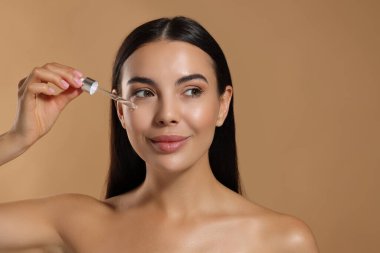 Güzel genç bir kadın bej arka planda yüzüne serum uyguluyor. Metin için boşluk