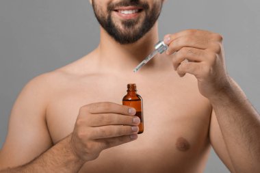 Gri arka planda kozmetik serumu olan adam, yakın plan.