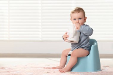 Tuvalet kağıdı rulosu olan küçük bir çocuk içeride plastik bebek lazımlığında oturuyor. Metin için boşluk