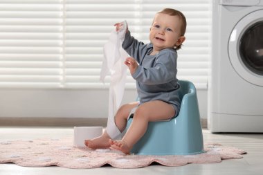 Tuvalet kağıdı rulosu olan küçük bir çocuk içeride plastik bebek lazımlığında oturuyor. Metin için boşluk