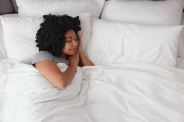 Güzel, genç bir kadın yumuşak yatakta uyuyor.