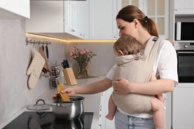 Anne, mutfakta makarna pişirirken çocuğunu askıda tutuyor.