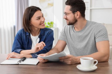 Evrakları olan genç bir çift içeride, ahşap masada emeklilik planlarını tartışıyor.
