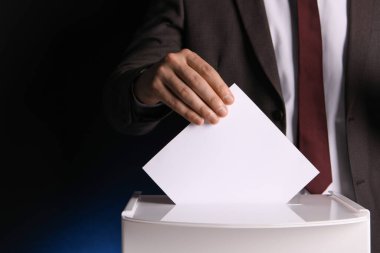 Adam oyunu koyu mavi arka planda oy sandığına koyuyor, yakın plan. Metin için boşluk