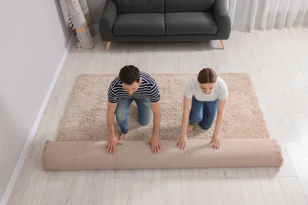 Couple unrolling carpet on floor in room