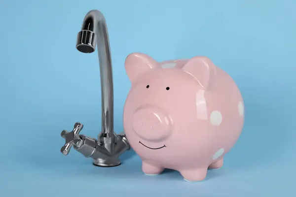 Water scarcity concept. Piggy bank and tap on light blue background