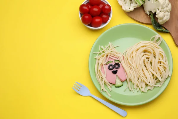 Creative serving for kids. Plate with cute dog made of tasty pasta, sausage and cucumber on yellow table, flat lay. Space for text