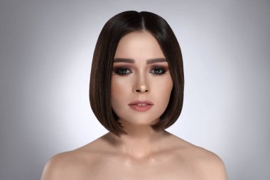 Gri arka planda kahverengi saçlı güzel bir genç kadının portresi.