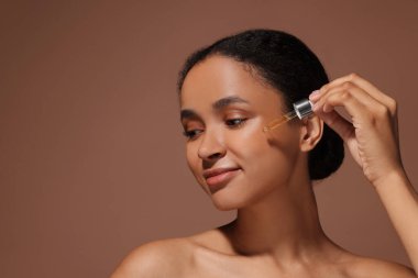 Kahverengi arka planda yüzüne serum süren güzel bir kadın. Metin için boşluk
