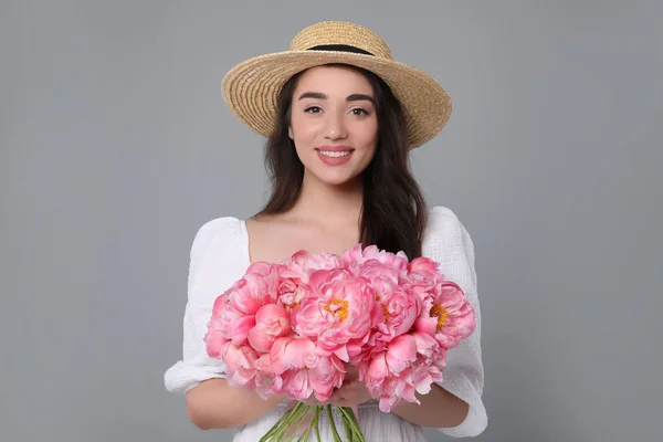 美しいです若いです女性でわら帽子でピンク牡丹の花束とともにグレーの背景 — ストック写真
