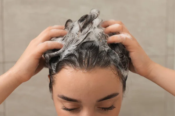 Woman washing hair with shampoo in shower, closeup