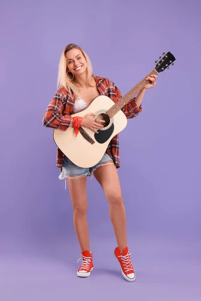 快乐的嬉皮士女人在紫色背景下弹奏吉他 — 图库照片
