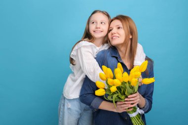 Anne ve güzel kızı açık mavi arka planda sarı lalelerle dolu bir buketle. Metin için boşluk