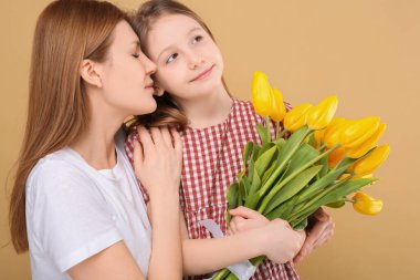 Anne ve güzel kızı bej arka planda sarı lale demetleriyle