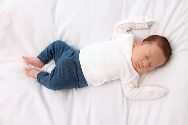 Cute newborn baby sleeping on white soft bed, top view