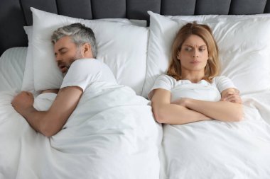 Evde yatakta horlayan kocasının yanında yatan sinirli kadın.