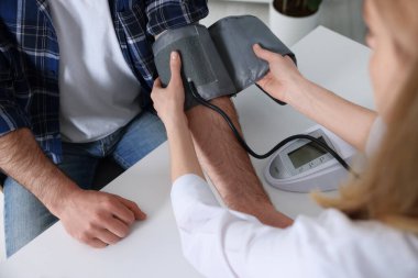 Doktor, masadaki adamın kan basıncını ölçüyor.