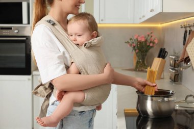 Anne, mutfakta makarna pişirirken çocuğunu askıda tutuyor.