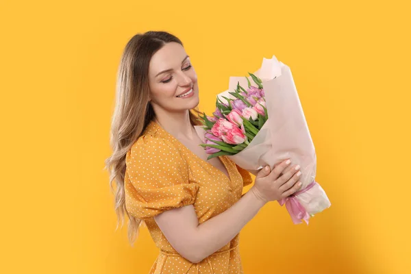 黄色の背景に美しいチューリップの花束を持つ幸せな若い女性 — ストック写真