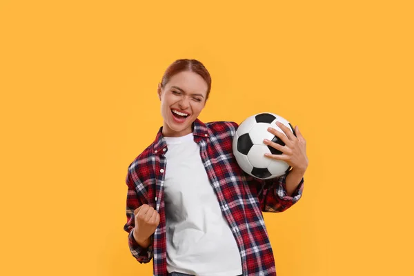 Emotional fan holding football ball and celebrating on yellow background