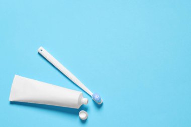 Açık mavi zemin üzerinde tutkal ve tüp bulunan plastik diş fırçası, düz. Metin için boşluk